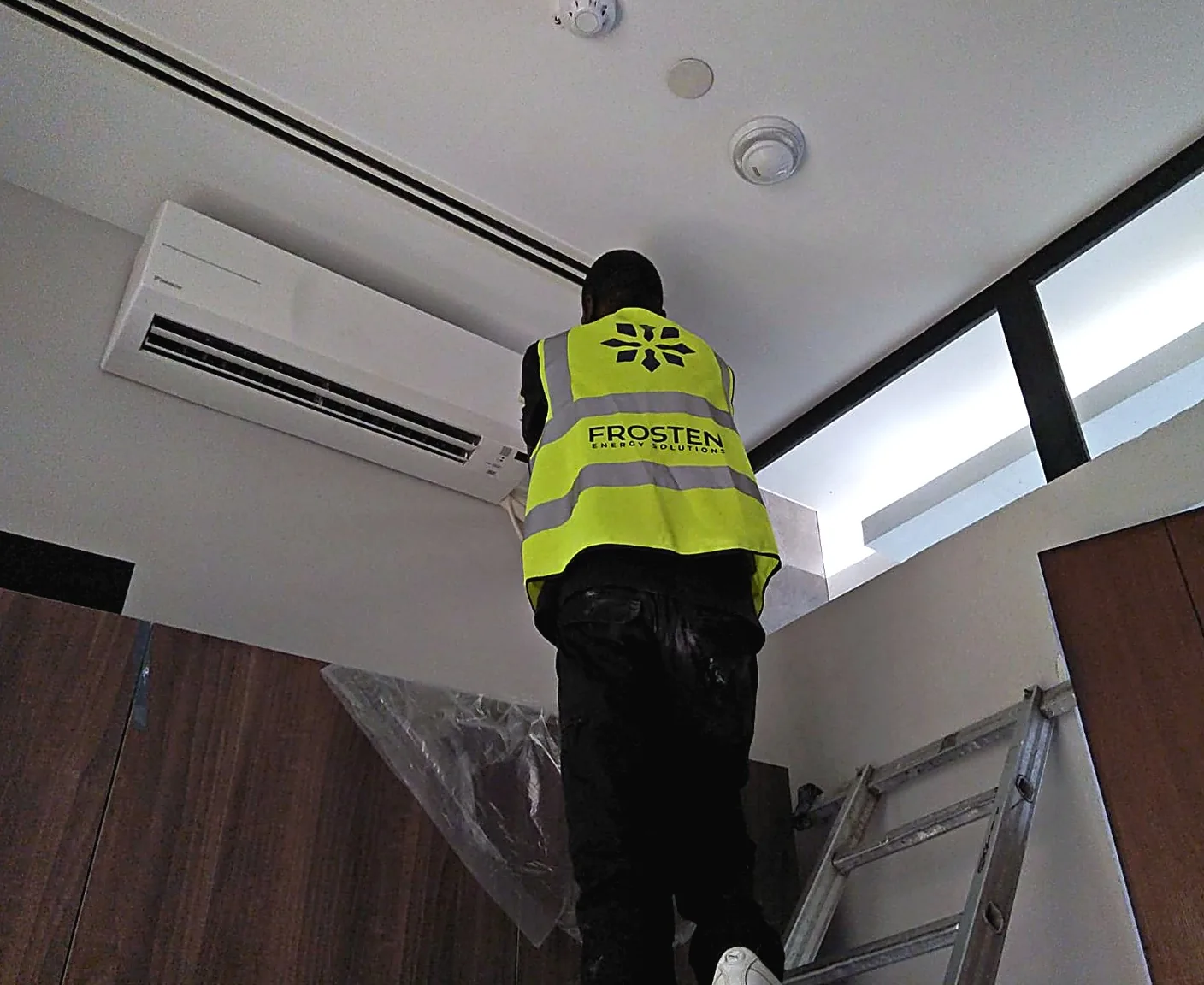 Frosten technician installing an indoor air conditioning unit from a ladder