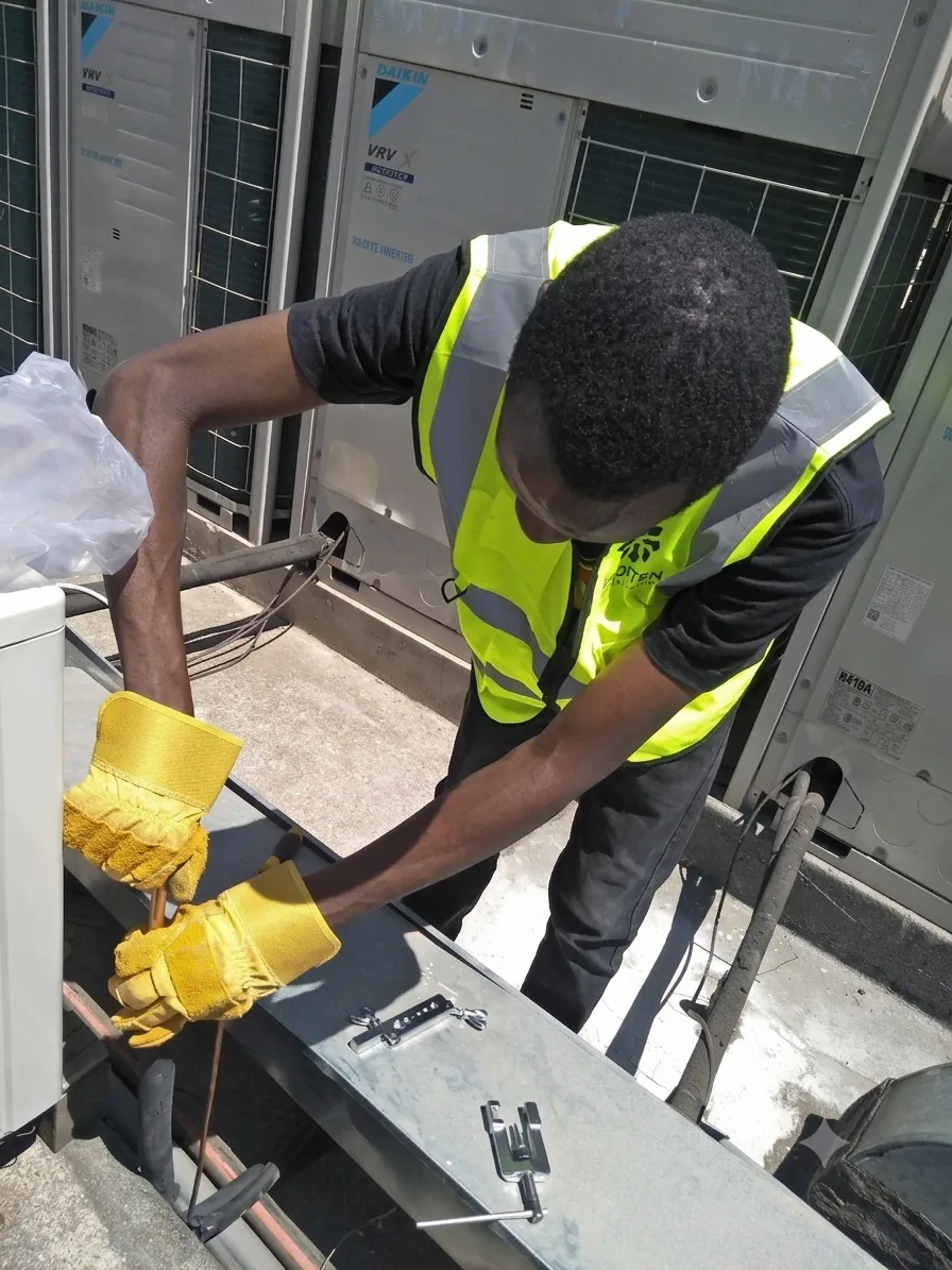 Frosten technician forming copper refrigerant pipework beside outdoor condensing units