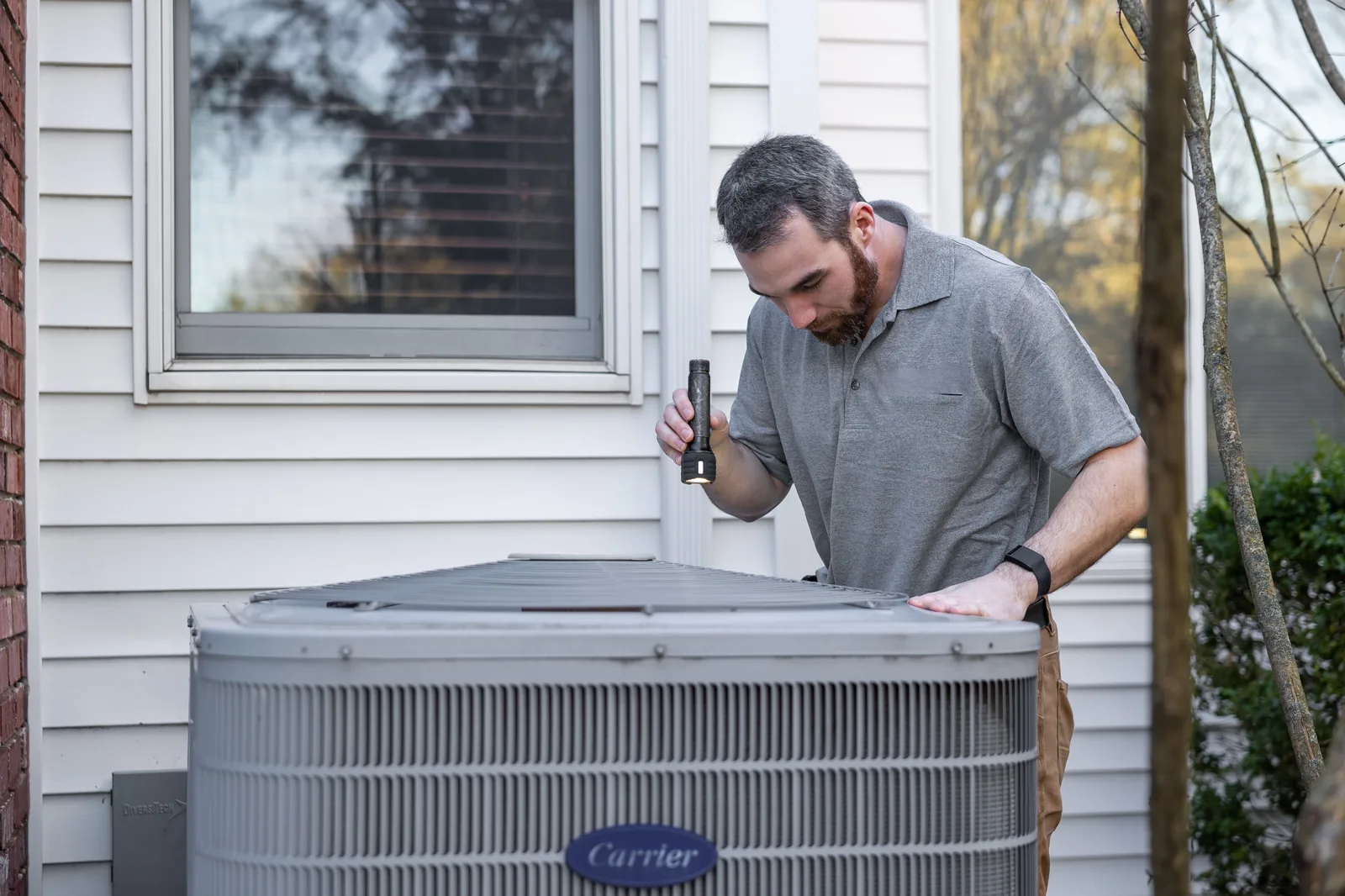 Engineer using a torch to inspect an outdoor condensing unit during a breakdown call-out